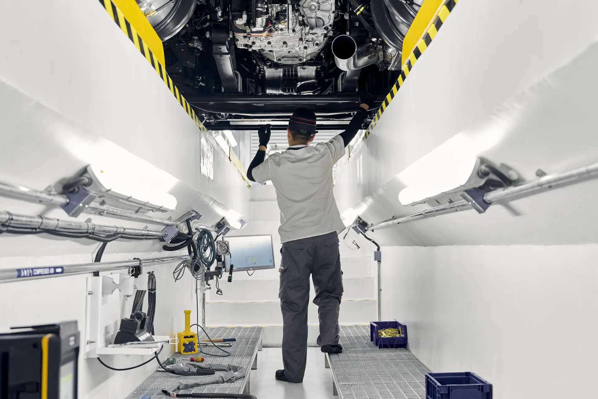 A technician inspecting a vehicle underside from a workshop inspection bay